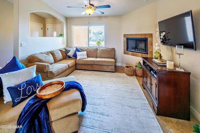 living room featuring ceiling fan, a tiled fireplace, arched walkways, and baseboards