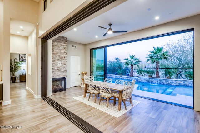 dining room with a stone fireplace, a towering ceiling, ceiling fan, and light hardwood / wood-style flooring