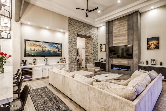 living room with ceiling fan, bar, wine cooler, a large fireplace, and light wood-type flooring