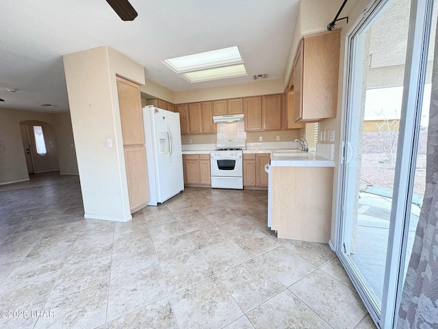 kitchen with visible vents, under cabinet range hood, arched walkways, white appliances, and a sink