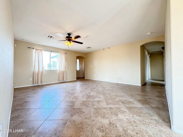 empty room with visible vents, arched walkways, baseboards, and a ceiling fan