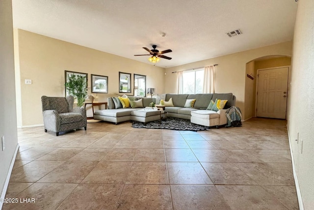 living area featuring visible vents, a ceiling fan, arched walkways, tile patterned flooring, and baseboards