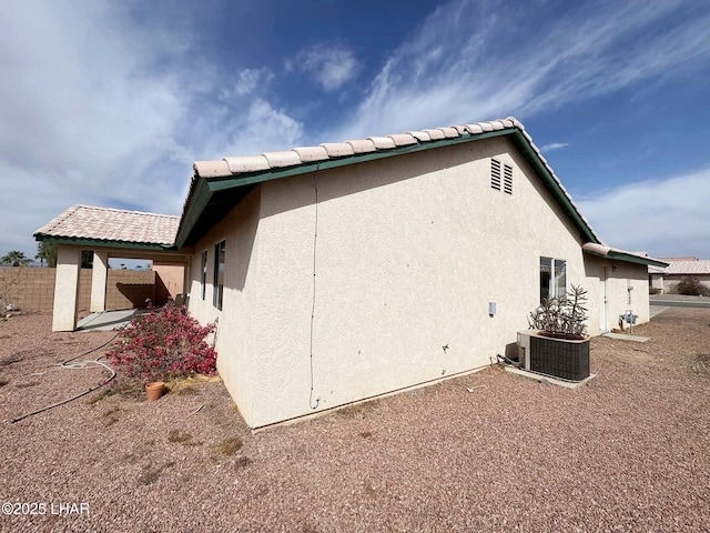 view of home's exterior featuring cooling unit, fence, a tile roof, and stucco siding