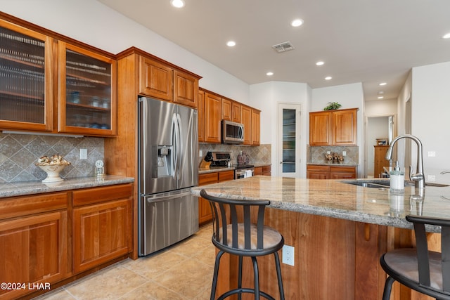 kitchen featuring sink, a kitchen island with sink, stainless steel appliances, a kitchen breakfast bar, and light stone countertops