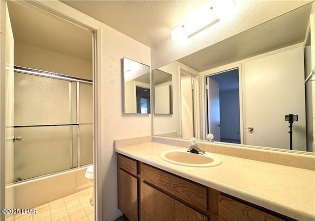 full bathroom with vanity, bath / shower combo with glass door, toilet, and a textured ceiling