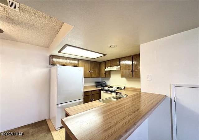 kitchen with sink, white appliances, kitchen peninsula, and a textured ceiling