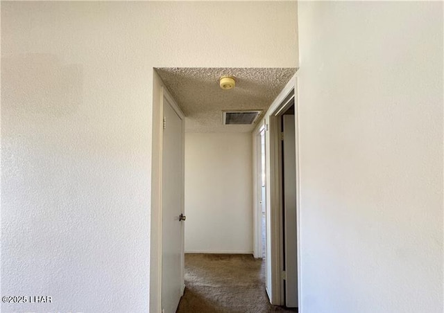 corridor with a textured ceiling and dark colored carpet