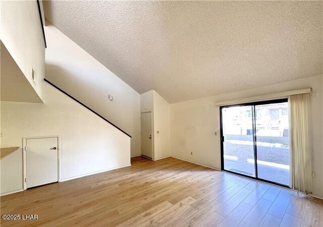 empty room with high vaulted ceiling, light carpet, and a textured ceiling