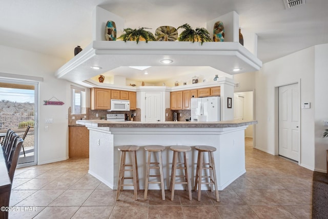 kitchen with white appliances, a kitchen bar, light countertops, and backsplash