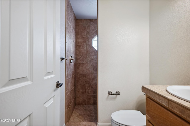 full bath with toilet, a textured wall, tiled shower, and vanity