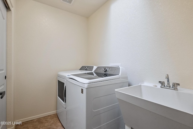 washroom with washing machine and clothes dryer, light tile patterned floors, visible vents, a sink, and laundry area