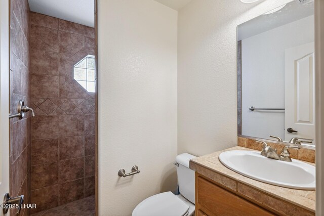 full bathroom with a tile shower, vanity, and toilet