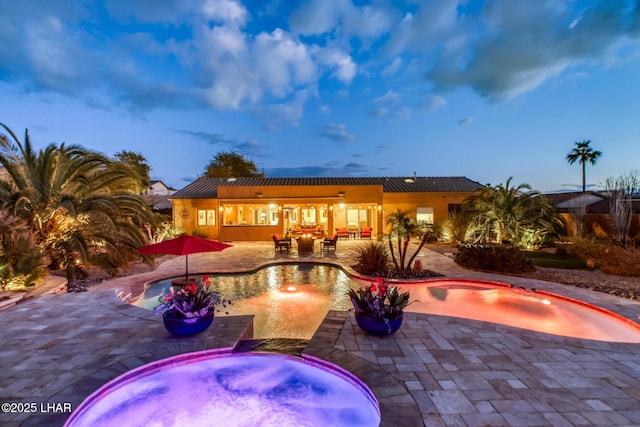 pool at dusk with a patio and an in ground hot tub