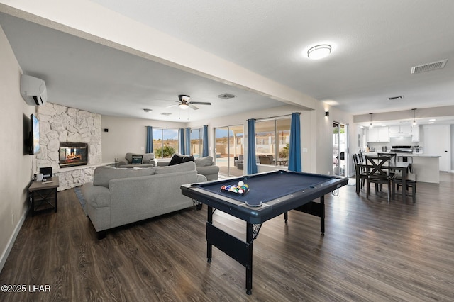 rec room featuring an AC wall unit, dark wood-style flooring, a stone fireplace, and visible vents