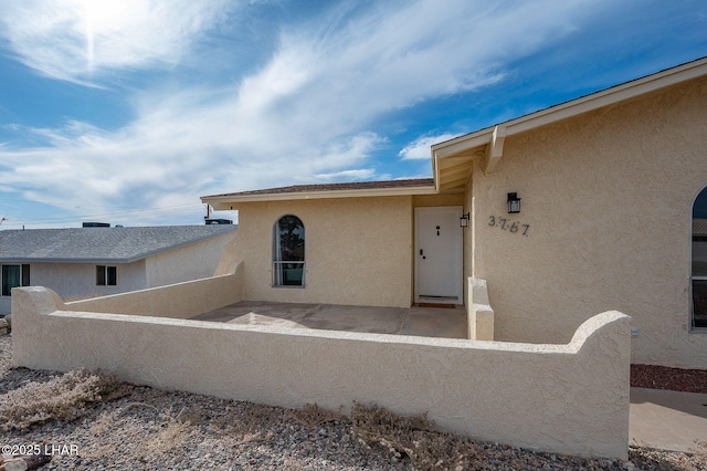 entrance to property with a patio area, stucco siding, and fence