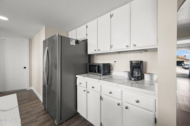 kitchen with light stone countertops, a textured ceiling, white cabinets, dark wood finished floors, and appliances with stainless steel finishes