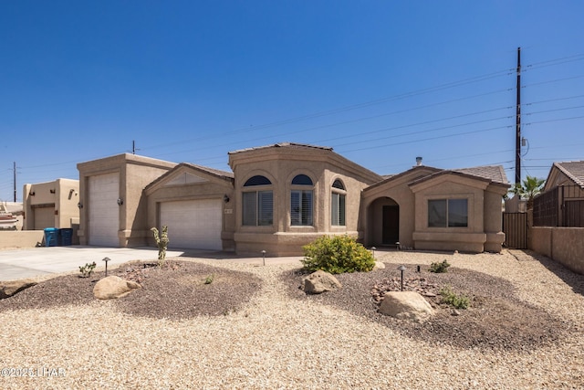 mediterranean / spanish house featuring concrete driveway, an attached garage, fence, and stucco siding