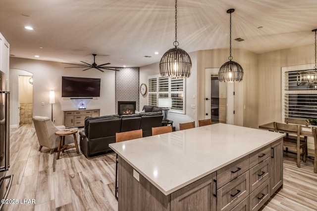 kitchen featuring arched walkways, decorative light fixtures, light countertops, light wood-type flooring, and a fireplace