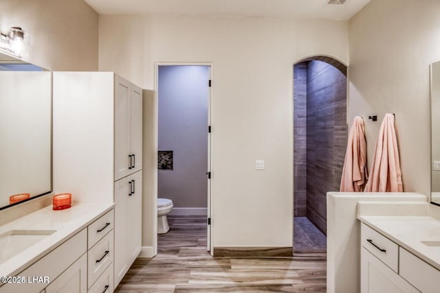 bathroom with visible vents, toilet, two vanities, wood finished floors, and a sink