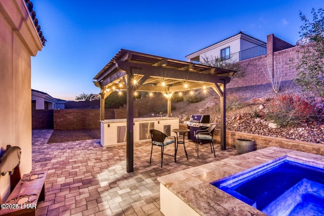 patio terrace at dusk featuring a fenced backyard, a jacuzzi, and area for grilling