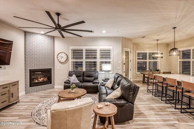 living room with recessed lighting, a tiled fireplace, light wood-style floors, baseboards, and ceiling fan with notable chandelier