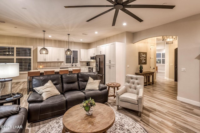 living area featuring arched walkways, recessed lighting, baseboards, and light wood-style floors