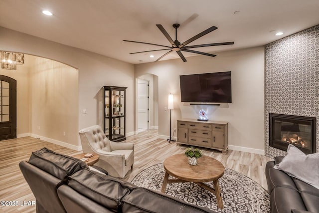 living room featuring baseboards, arched walkways, a tiled fireplace, light wood-style floors, and recessed lighting