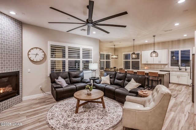 living room with ceiling fan, a tile fireplace, recessed lighting, baseboards, and light wood-style floors