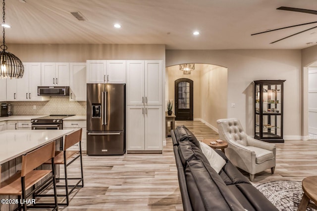 kitchen featuring arched walkways, white cabinets, appliances with stainless steel finishes, hanging light fixtures, and light countertops