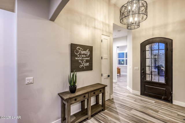 foyer entrance with arched walkways, a notable chandelier, wood finished floors, and baseboards