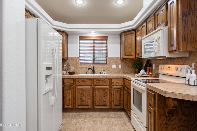 kitchen featuring sink, white appliances, light tile patterned floors, backsplash, and a tray ceiling