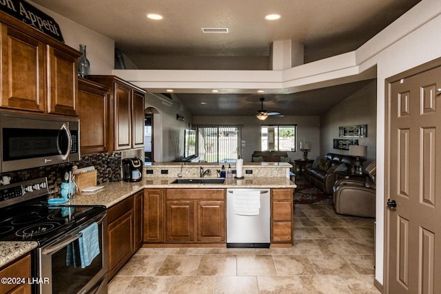 kitchen featuring sink, appliances with stainless steel finishes, light stone counters, decorative backsplash, and kitchen peninsula