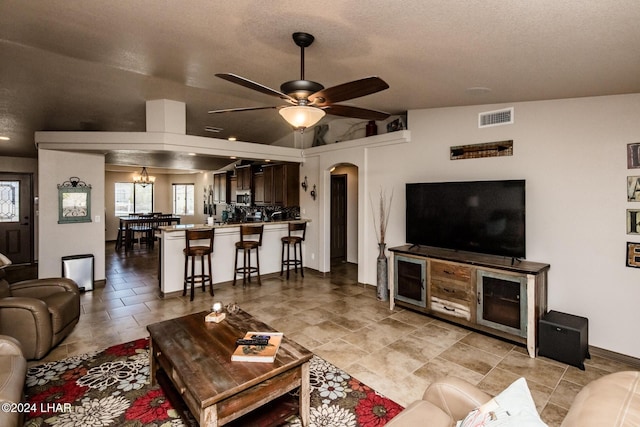 living room with ceiling fan with notable chandelier, vaulted ceiling, and a textured ceiling