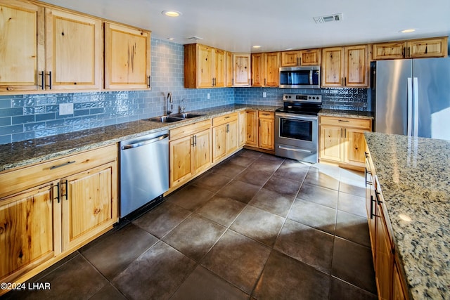 kitchen with sink, stainless steel appliances, light stone counters, dark tile patterned flooring, and decorative backsplash