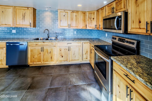 kitchen featuring sink, dark tile patterned floors, stone counters, appliances with stainless steel finishes, and light brown cabinetry