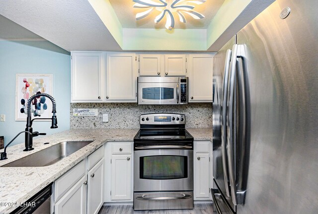 kitchen featuring sink, white cabinetry, stainless steel appliances, light stone countertops, and decorative backsplash