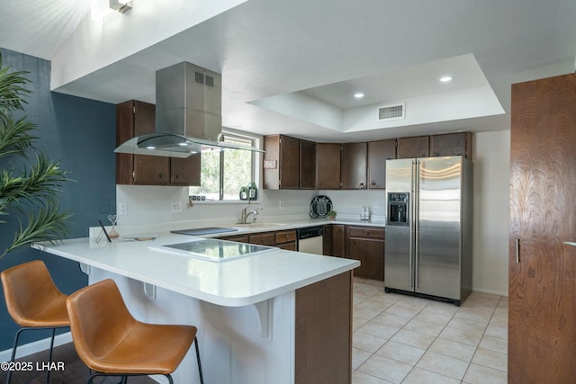 kitchen featuring a tray ceiling, stainless steel refrigerator with ice dispenser, a peninsula, and wall chimney range hood