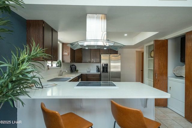 kitchen featuring black electric stovetop, light countertops, island range hood, washer / dryer, and stainless steel fridge with ice dispenser