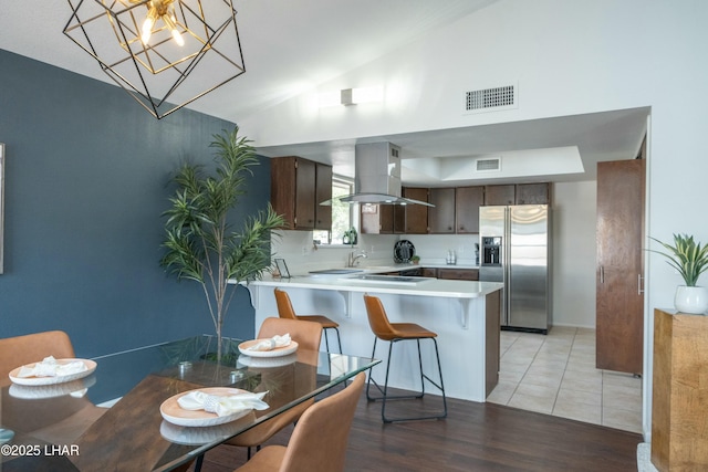 kitchen featuring stainless steel refrigerator with ice dispenser, light countertops, visible vents, dark brown cabinets, and island range hood