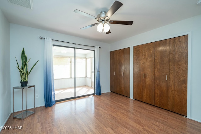 unfurnished bedroom with a ceiling fan, visible vents, multiple closets, and wood finished floors