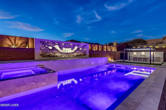 pool at dusk featuring exterior kitchen, an in ground hot tub, and exterior bar