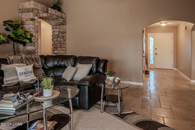 living area with arched walkways, baseboards, and stone tile floors