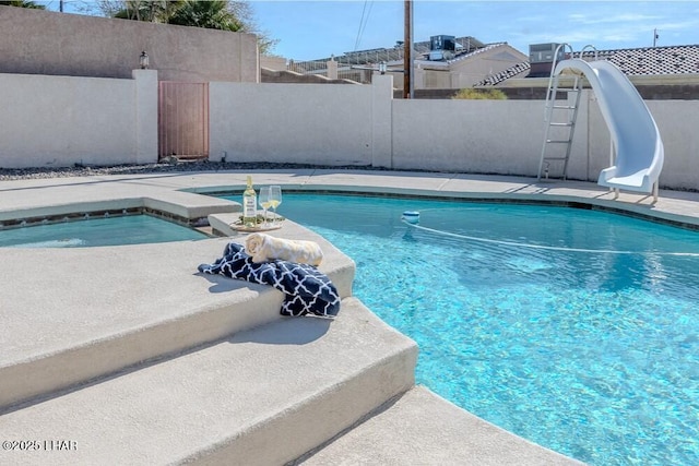 view of swimming pool with a fenced in pool, a water slide, fence, and an in ground hot tub