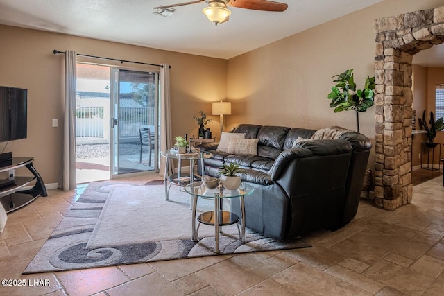 living area with baseboards, visible vents, a ceiling fan, and stone tile flooring