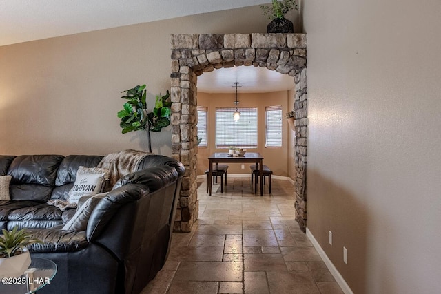 living room with arched walkways, stone tile flooring, and baseboards