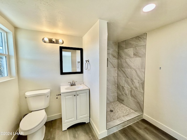 bathroom featuring vanity, wood-type flooring, toilet, and tiled shower