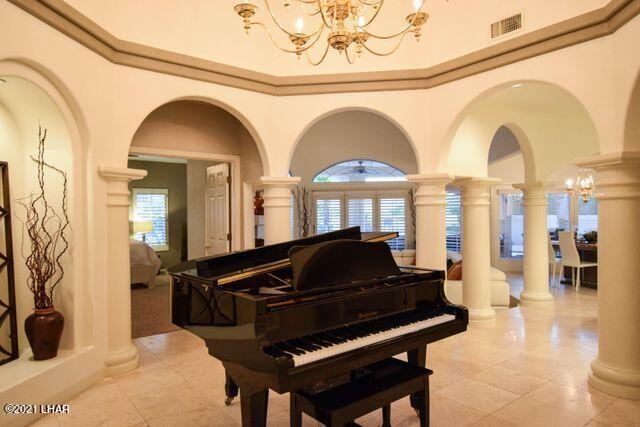 miscellaneous room with crown molding, light tile patterned floors, an inviting chandelier, and ornate columns