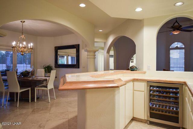 bar featuring beverage cooler, decorative light fixtures, ceiling fan with notable chandelier, and light tile patterned floors