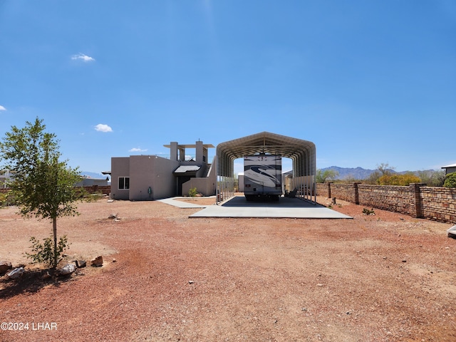 rear view of house with stucco siding, a detached carport, dirt driveway, and fence