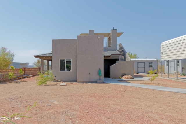 rear view of property featuring an outbuilding, stucco siding, a storage shed, and fence